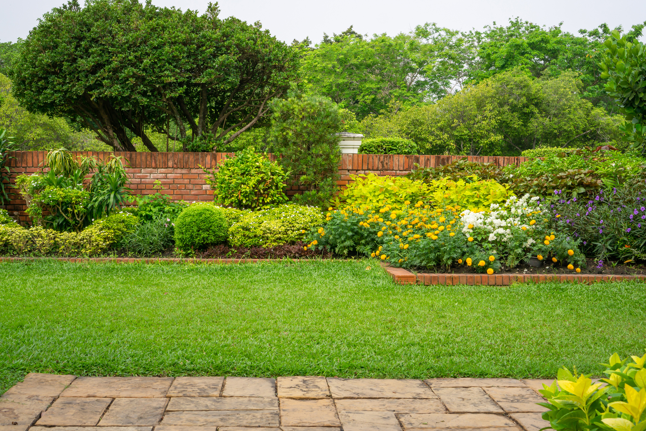 a green lawn and garden near a brick wall